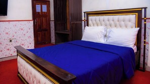 A bedroom with a large bed, a wooden wardrobe, and a television on the wall. - Hôtel La Rochelle  (Bonaberi)