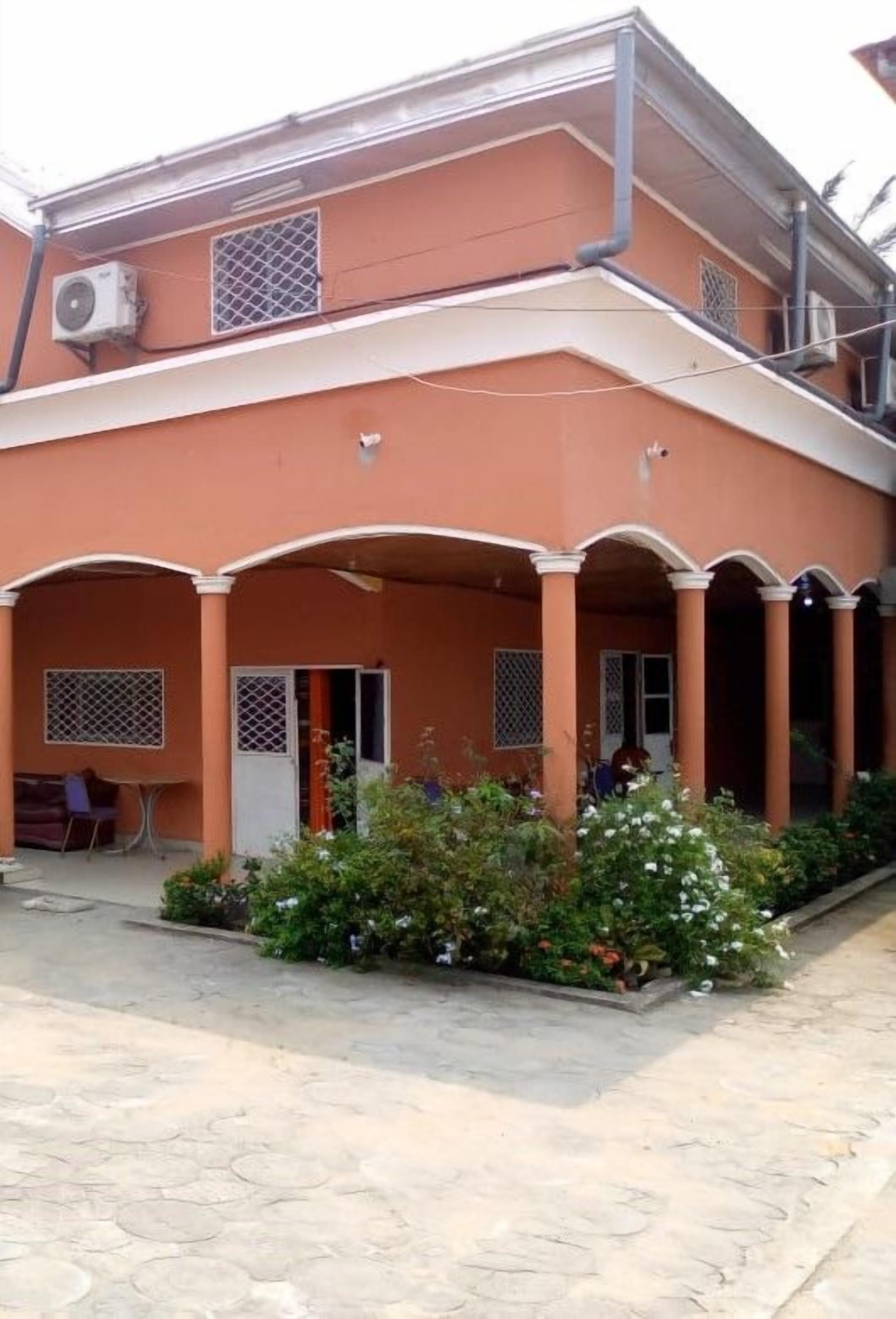 A building with a covered outdoor area, air conditioning units, and a small garden with flowers.