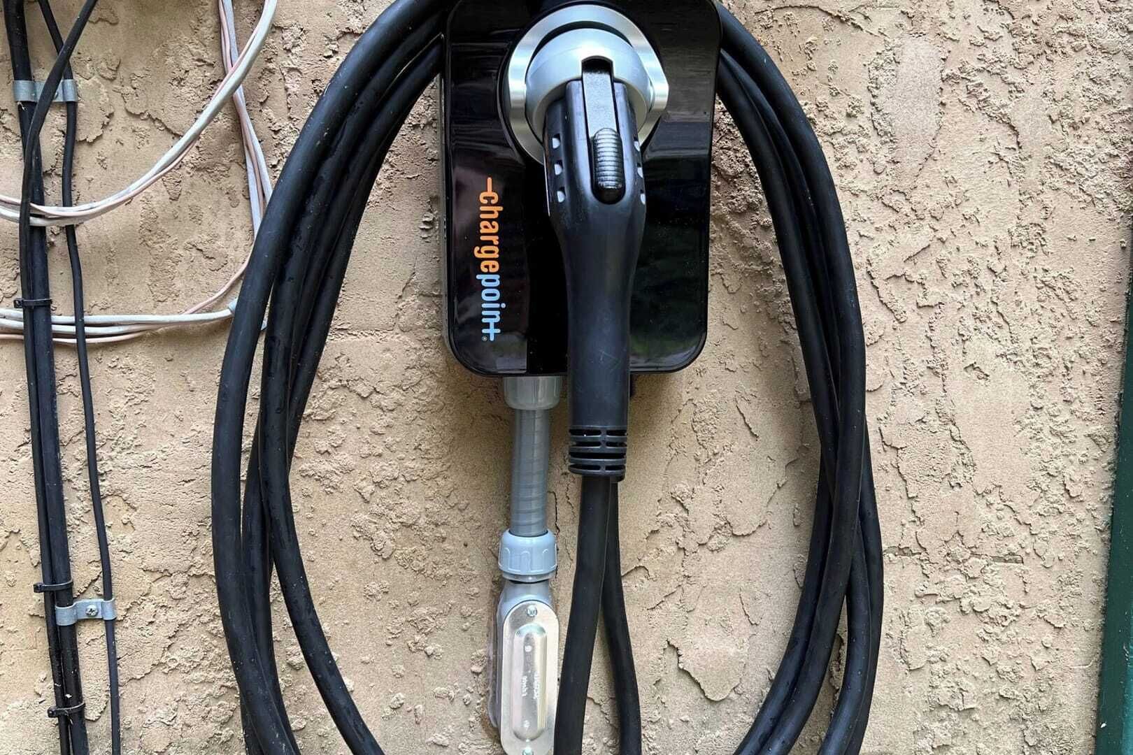 Une borne de recharge dotée d’un câble branché, fixée à un mur texturé.