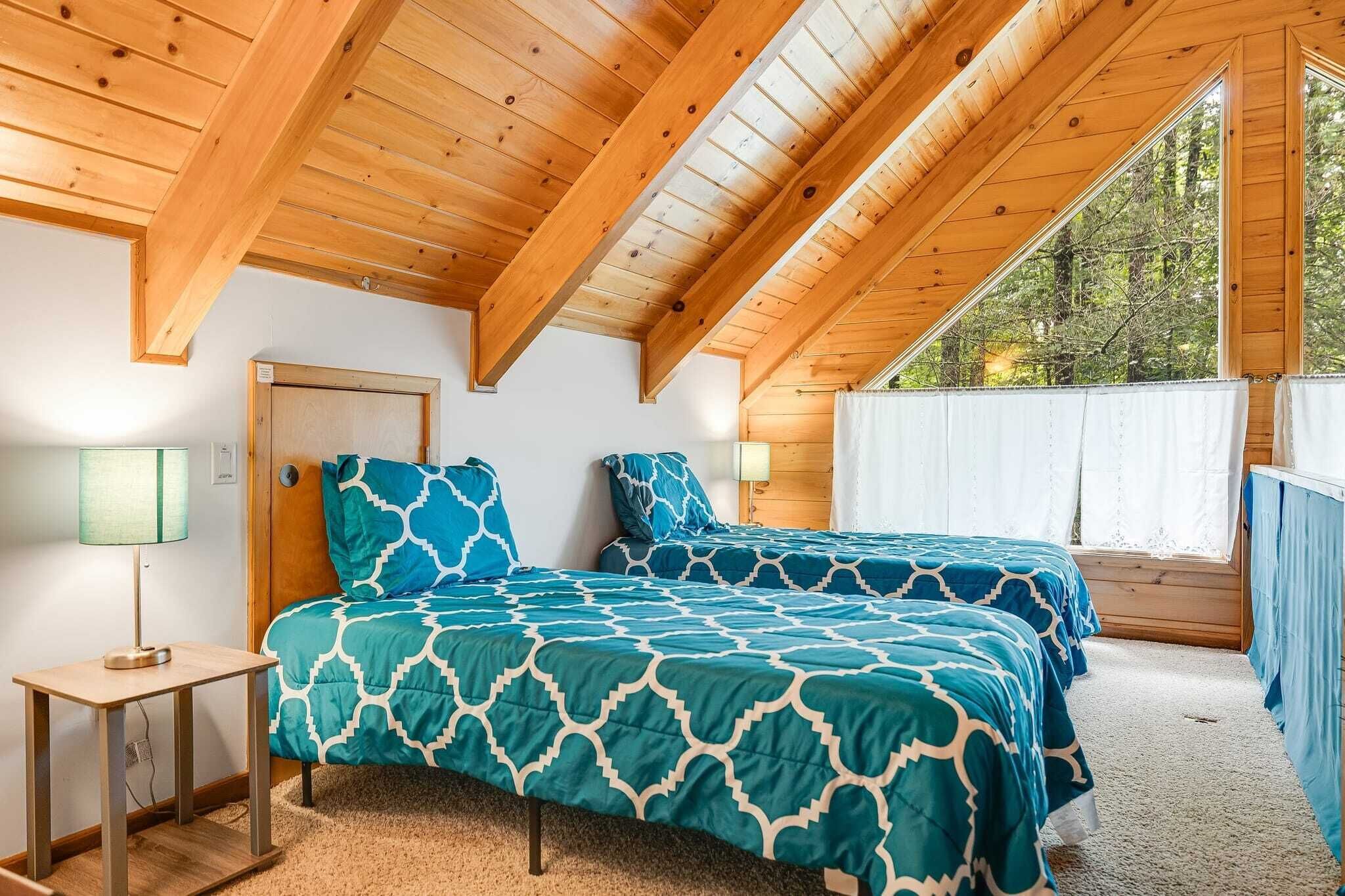 Une chambre avec deux lits, des poutres en bois, une fenêtre avec des rideaux et une table de chevet avec une lampe.