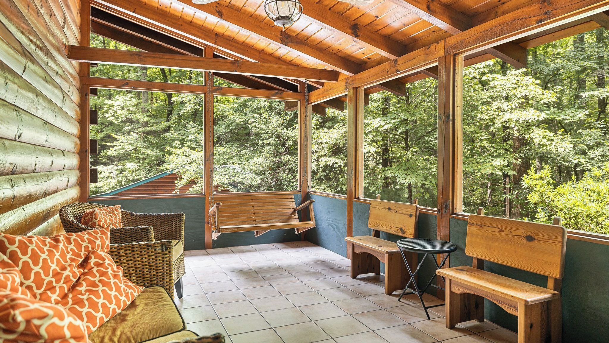 A wooden cabin with a porch, wicker furniture, and a view of the forest.