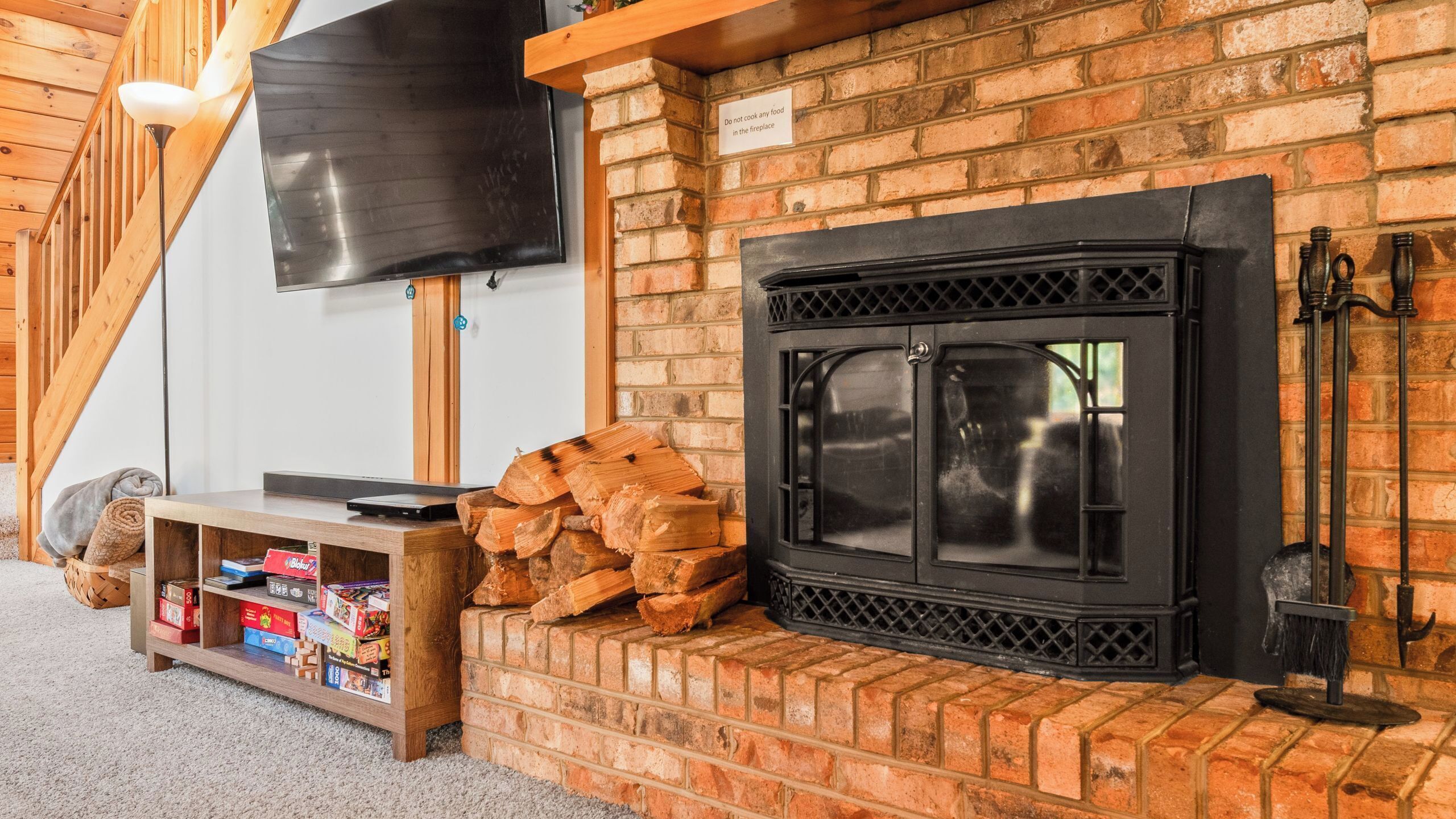 Una habitación acogedora con chimenea, televisor montado en la pared y una estantería de madera con libros y una manta.