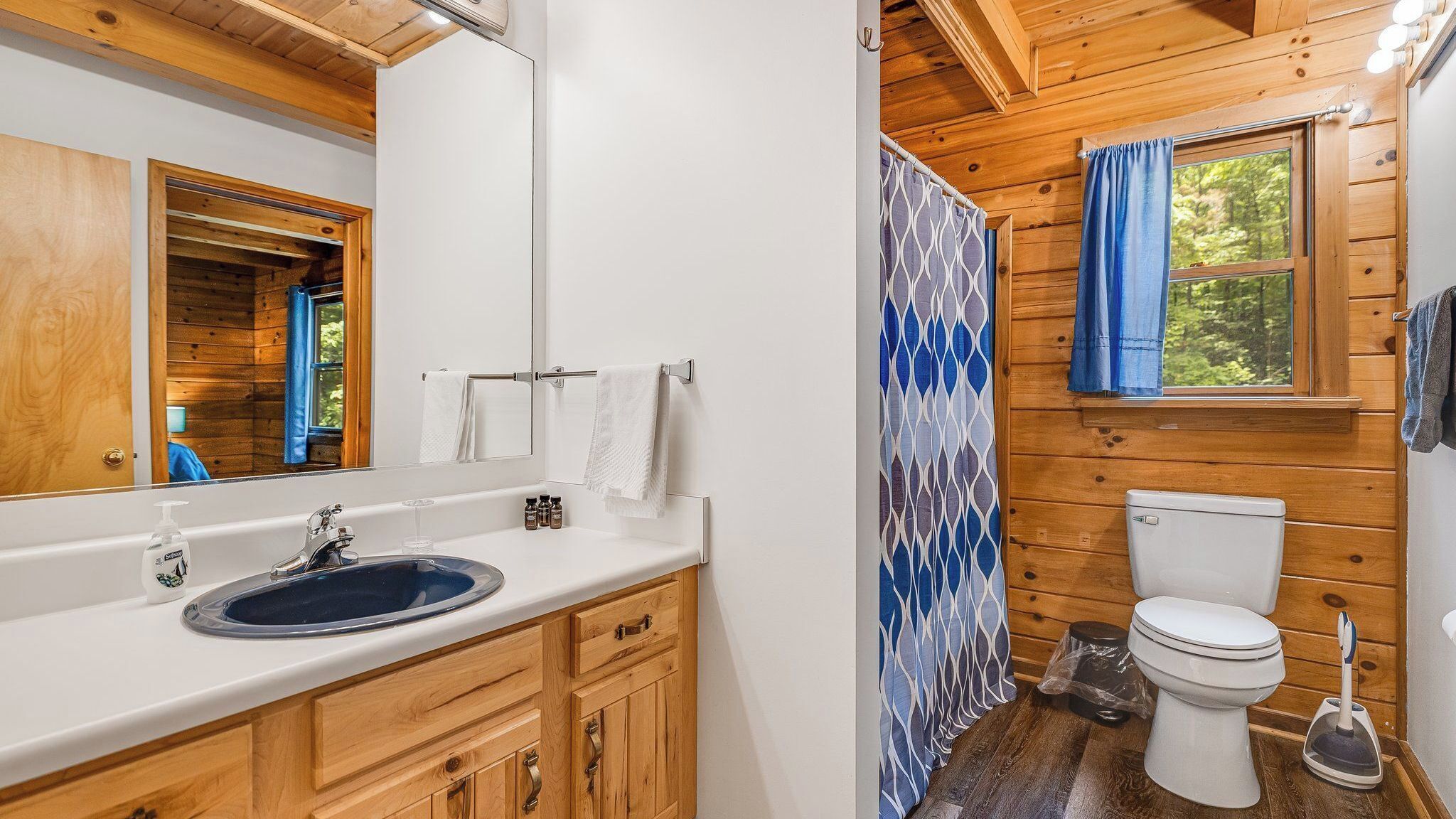 A wooden cabin bathroom with a sink, mirror, towel rack, toilet, and shower curtain.