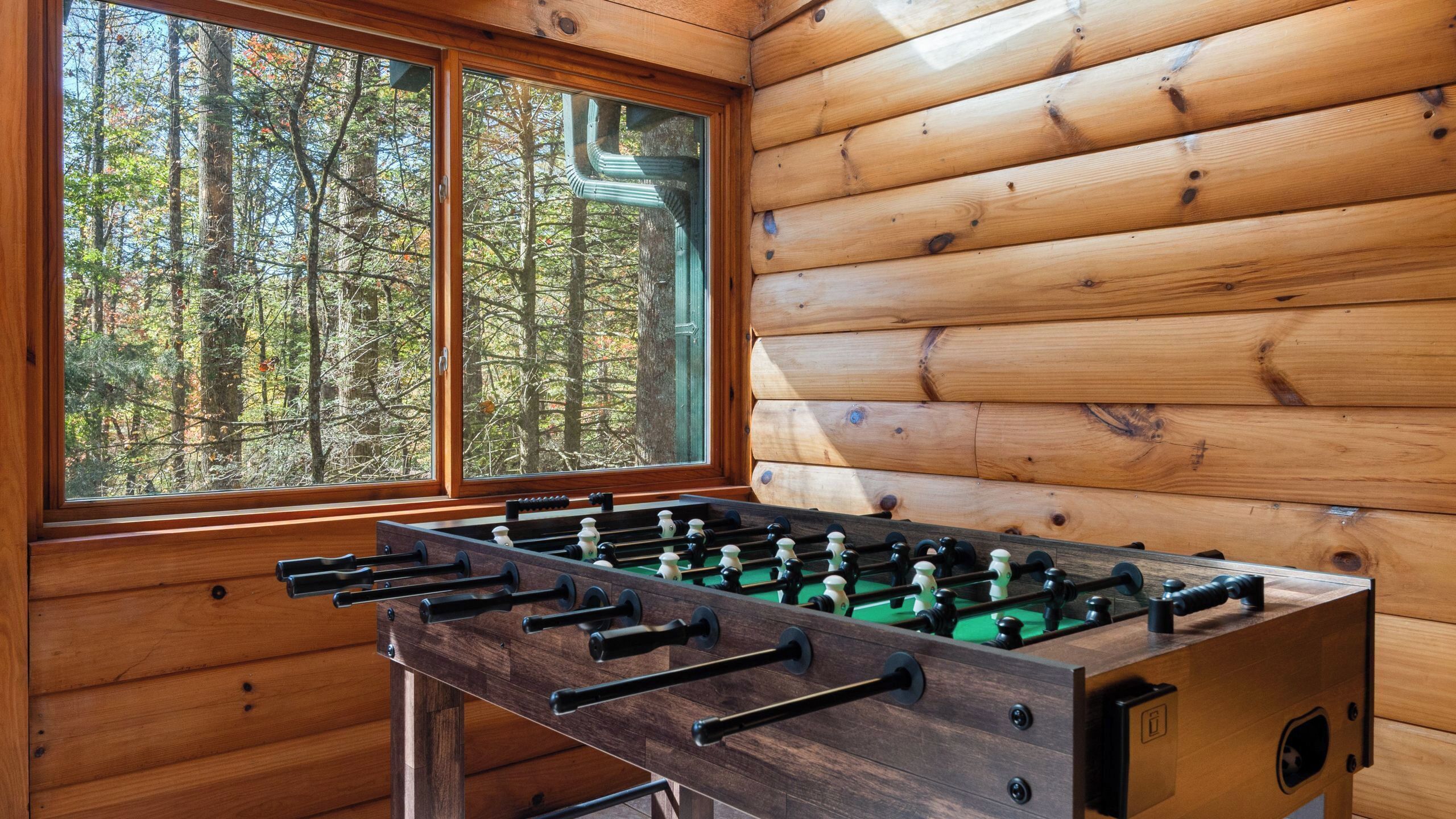 A wooden room with a foosball table and a window overlooking a forest.