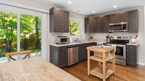 A modern kitchen with dark cabinets, stainless steel appliances, and a wooden table. - Little Sycamore by Avantstay Premier Location + Patio (Asheville)
