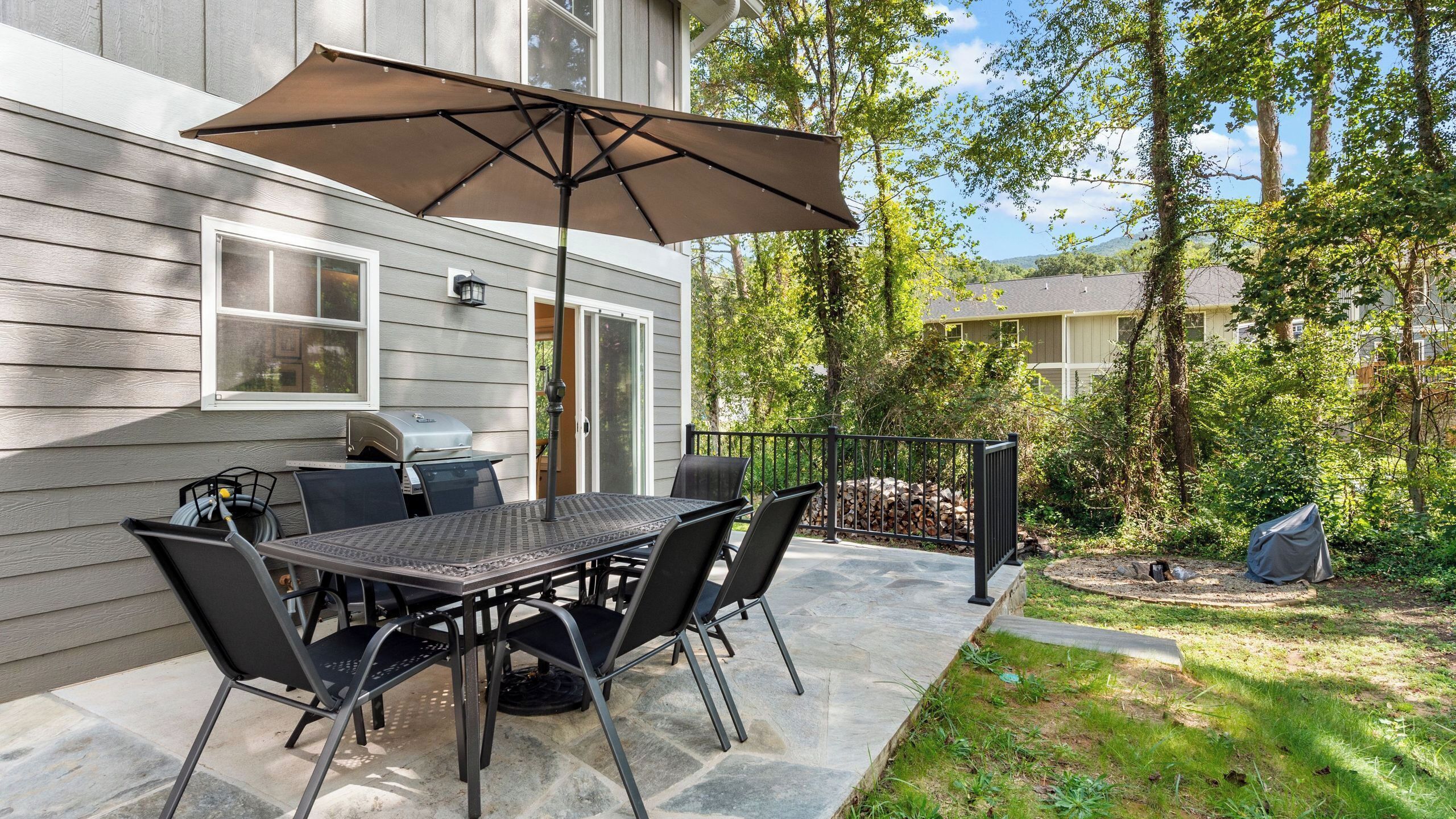 Une terrasse extérieure avec une table et des chaises, un barbecue et un grand parasol.