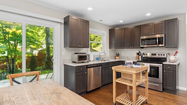 A modern kitchen with dark cabinets, stainless steel appliances, and a wooden table. - Little Sycamore by Avantstay Premier Location + Patio (Asheville)