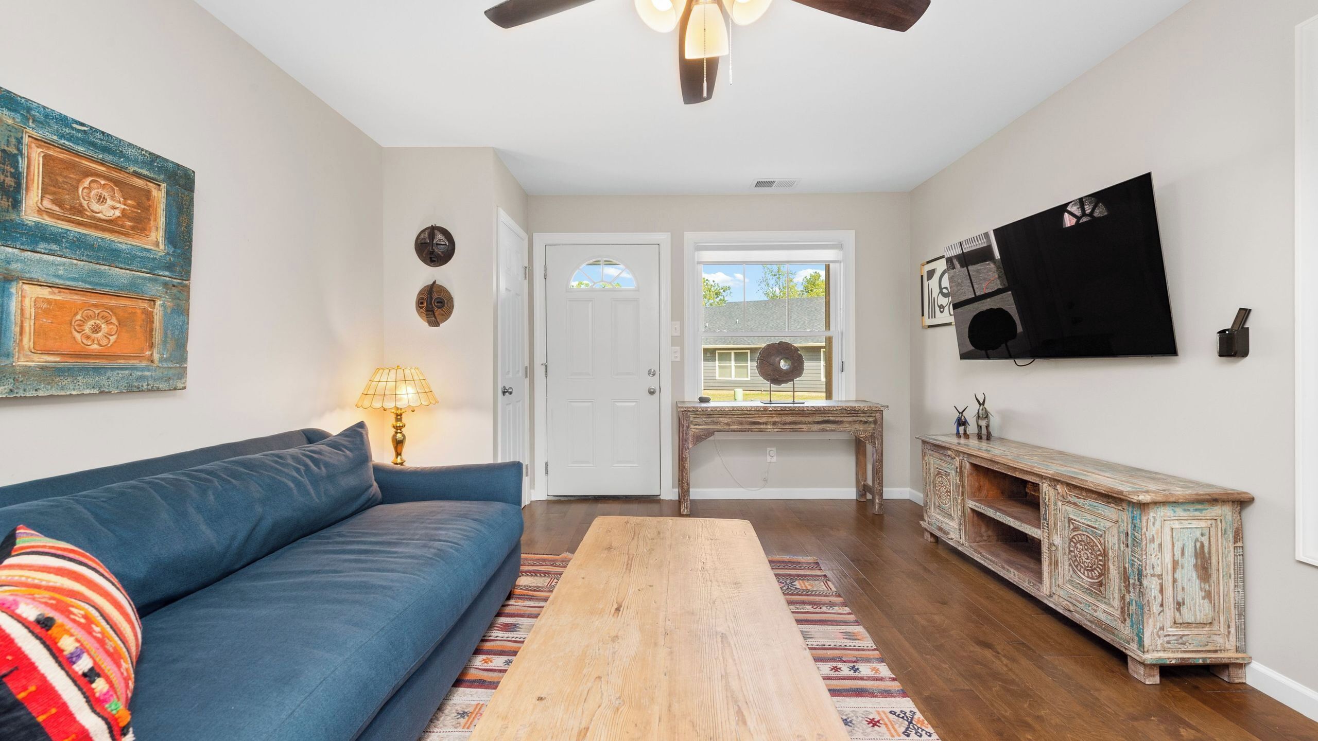 A living room with a blue sofa, a wooden coffee table, a patterned rug, a rustic sideboard, and a ceiling fan.