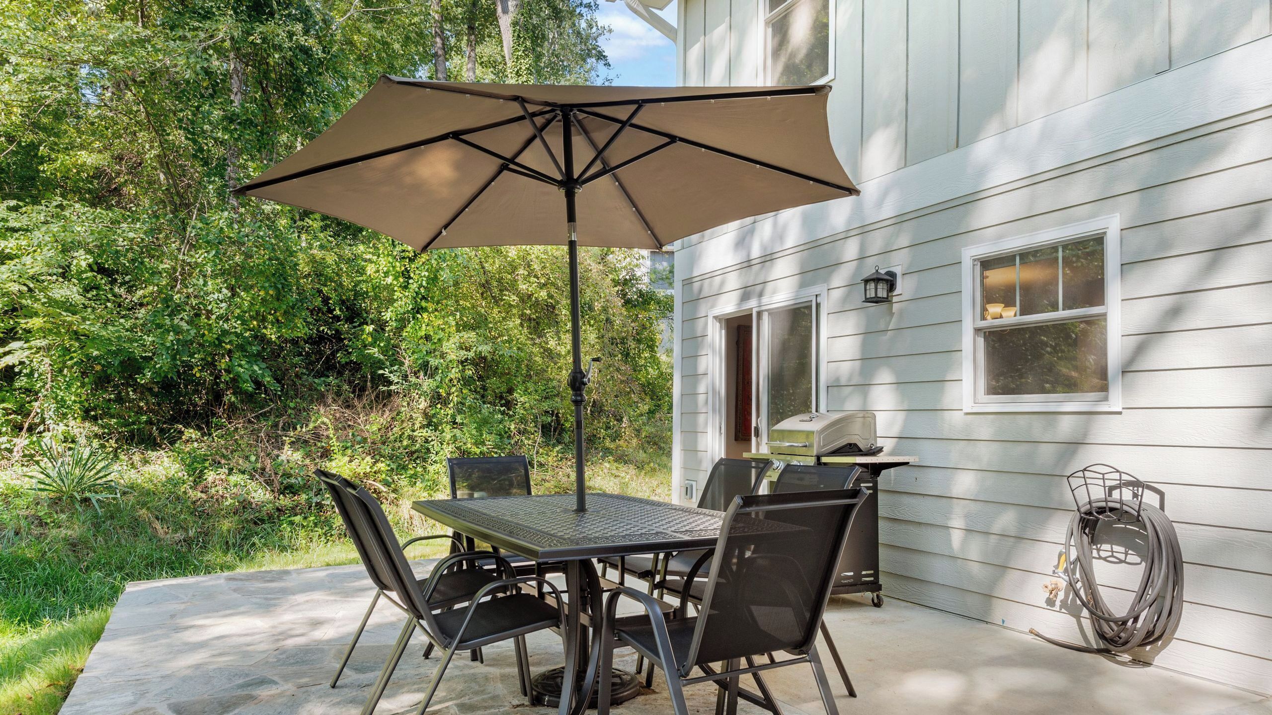 Un patio al aire libre con una mesa, sillas, una sombrilla grande y una parrilla.