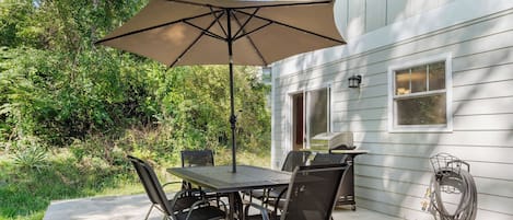 Un patio al aire libre con una mesa, sillas, una sombrilla grande y una parrilla.