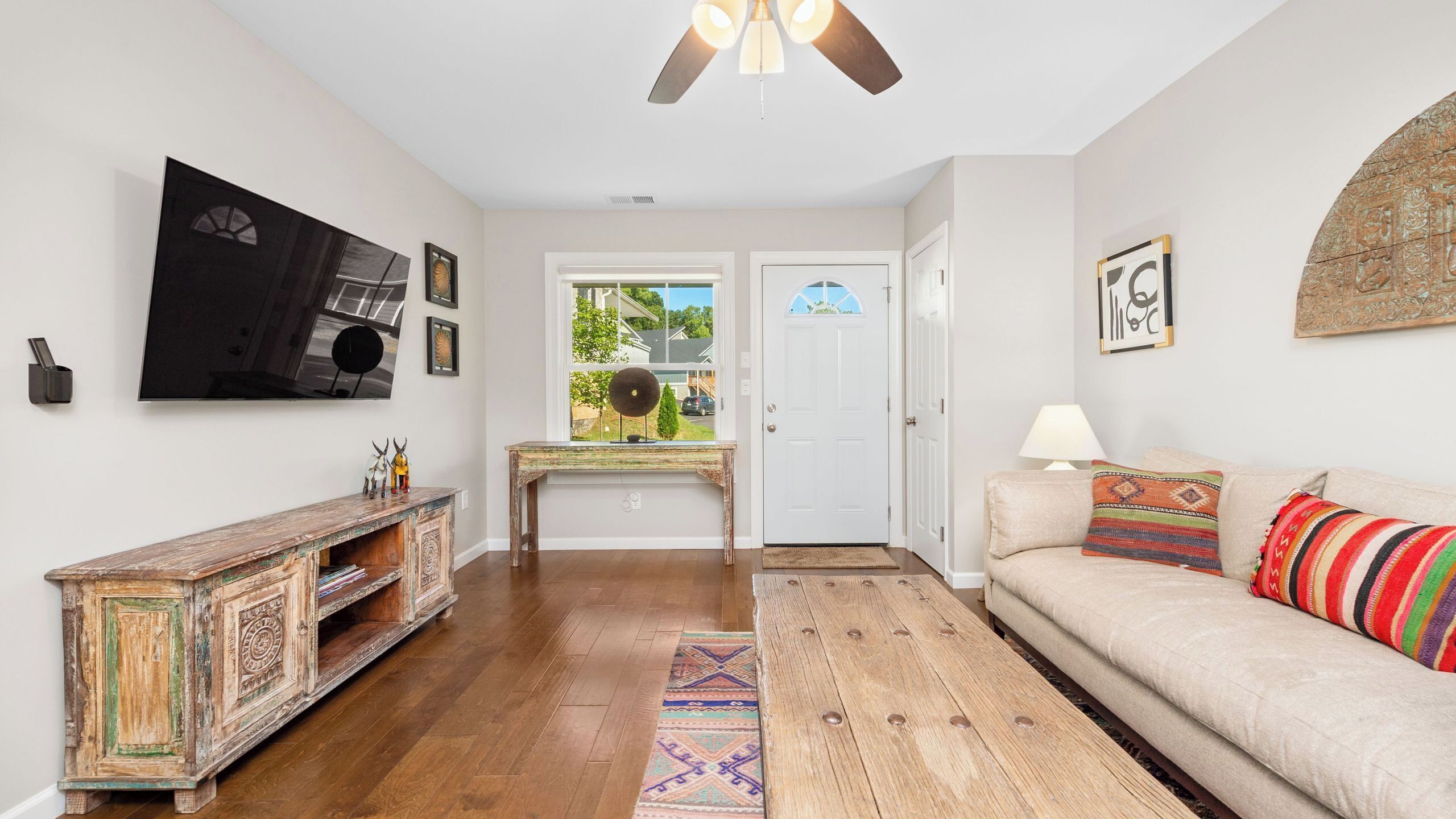 A living room with a wooden floor, a sofa, a TV, and a door leading outside.