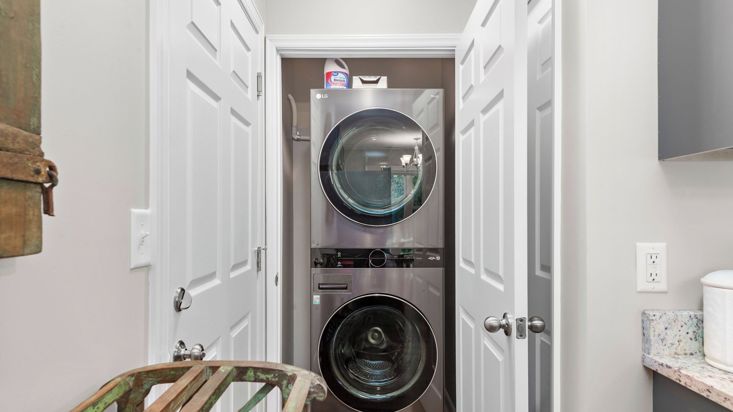 A laundry room with two stacked washing machines, a door with a handle, and a wall-mounted light fixture.