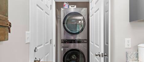 A laundry room with two stacked washing machines, a door with a handle, and a wall-mounted light fixture.