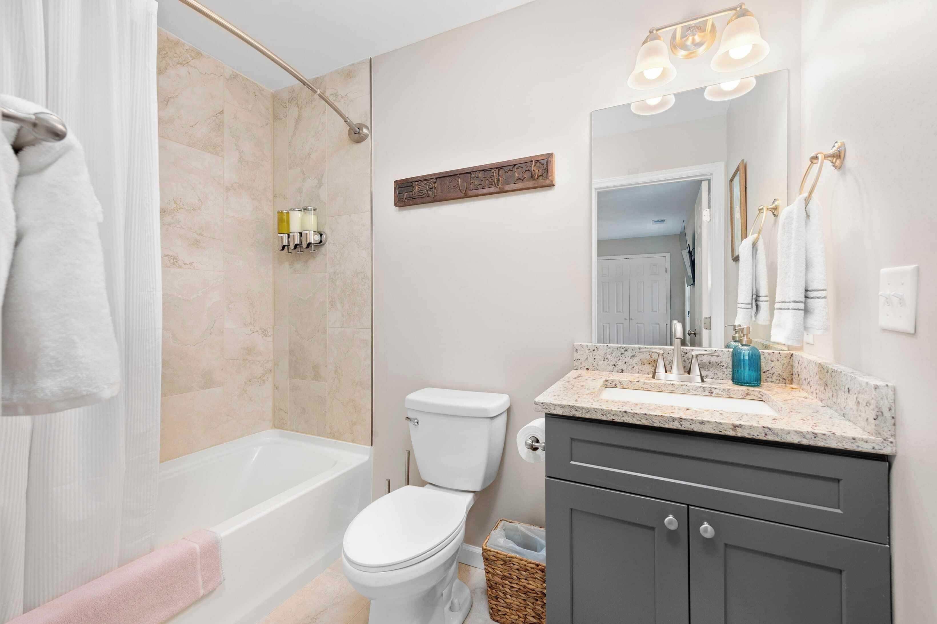 A modern bathroom with a bathtub, toilet, and a vanity with a sink and mirror.