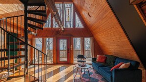 A spacious loft with a spiral staircase, a large window, a blue sofa, and a patterned rug. - Firepit + Mountain Views A-frame in Fairview Honeycomb Hideaway by Avantstay (Fairview)