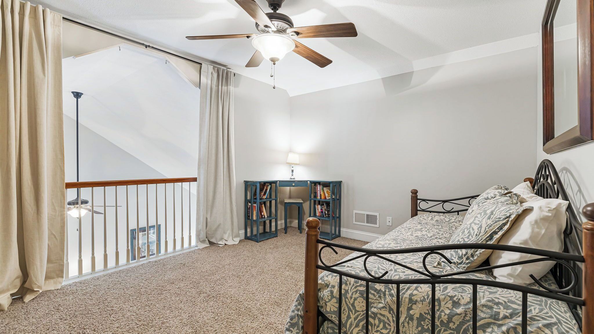A bedroom with a bed, a ceiling fan, a desk with books, and a view of a balcony.