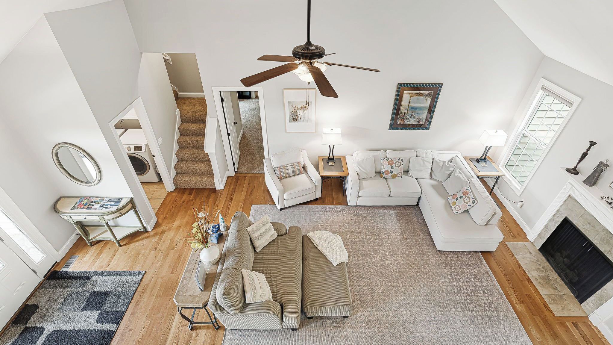 A spacious living room with a ceiling fan, a fireplace, and a staircase leading to an upper level.