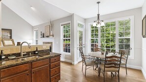 A kitchen with a granite countertop, wooden cabinets, a dining area with a table and chairs, and large windows with a view of greenery. - Fairview Vista by Avantstay 10 Mins to Asheville (Fairview)