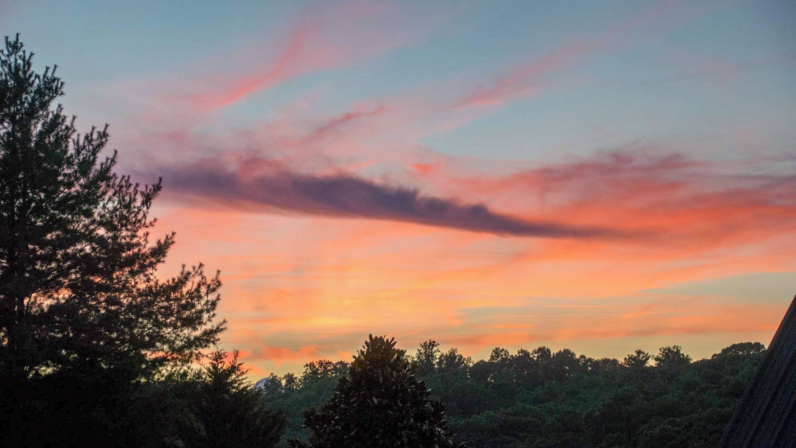 Ein Sonnenuntergangshimmel mit Wolken, Bäumen und einem Berg im Hintergrund.