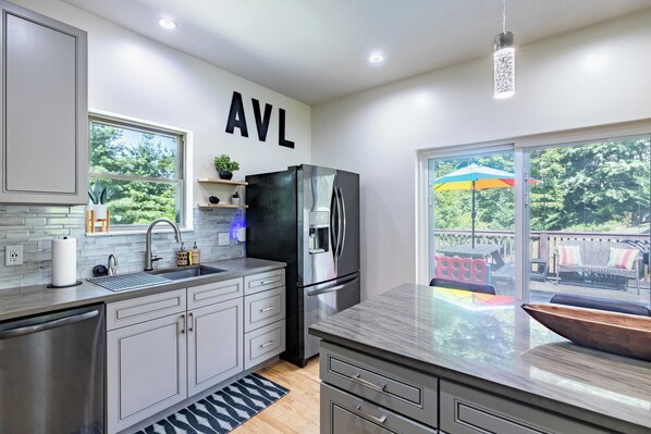 A modern kitchen with grey cabinets, a black refrigerator, and a large window overlooking a deck.