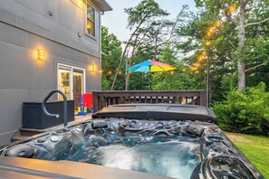 A hot tub with a wooden deck, surrounded by trees and string lights.