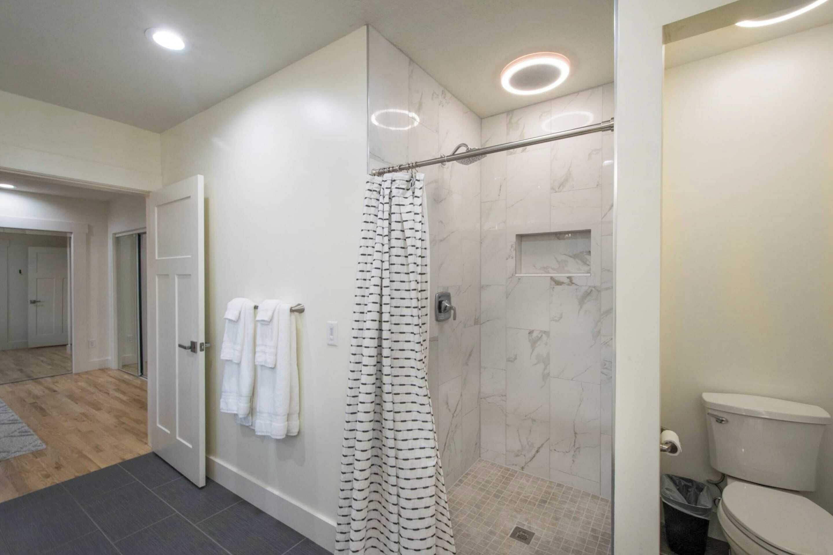 A modern bathroom with a shower, toilet, and a glass door leading to another room.