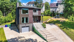 A modern two-story house with a garage, a covered porch, and a landscaped yard. - Hot Tub, Fire Pit, Mountain Views, 10min to AVL Modern Escape by Avanstay (Asheville)