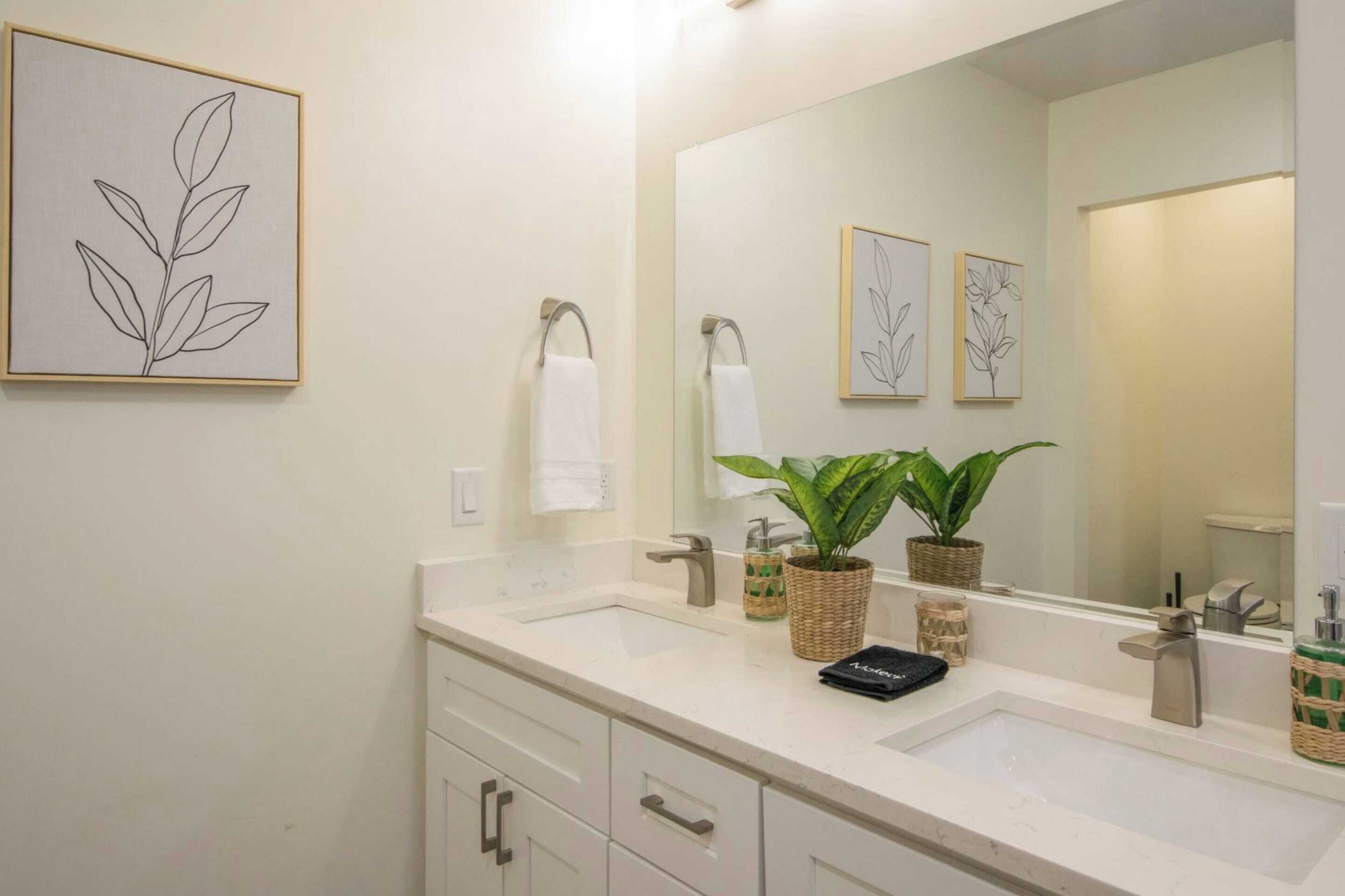A bathroom with two sinks, a large mirror, and framed botanical artwork on the wall.