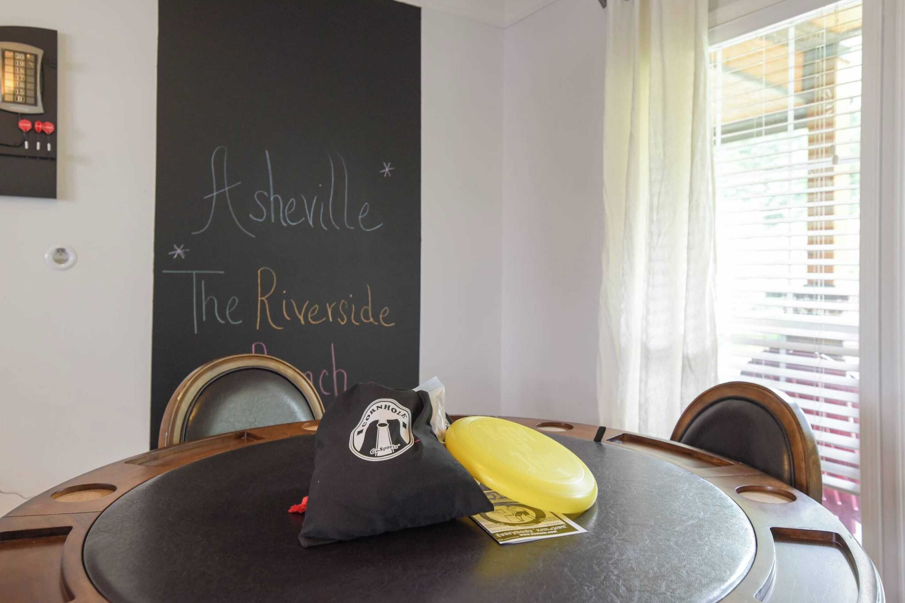 Una mesa redonda con un cojín negro, un objeto amarillo y una pizarra con la inscripción 'Asheville The Riverside'.