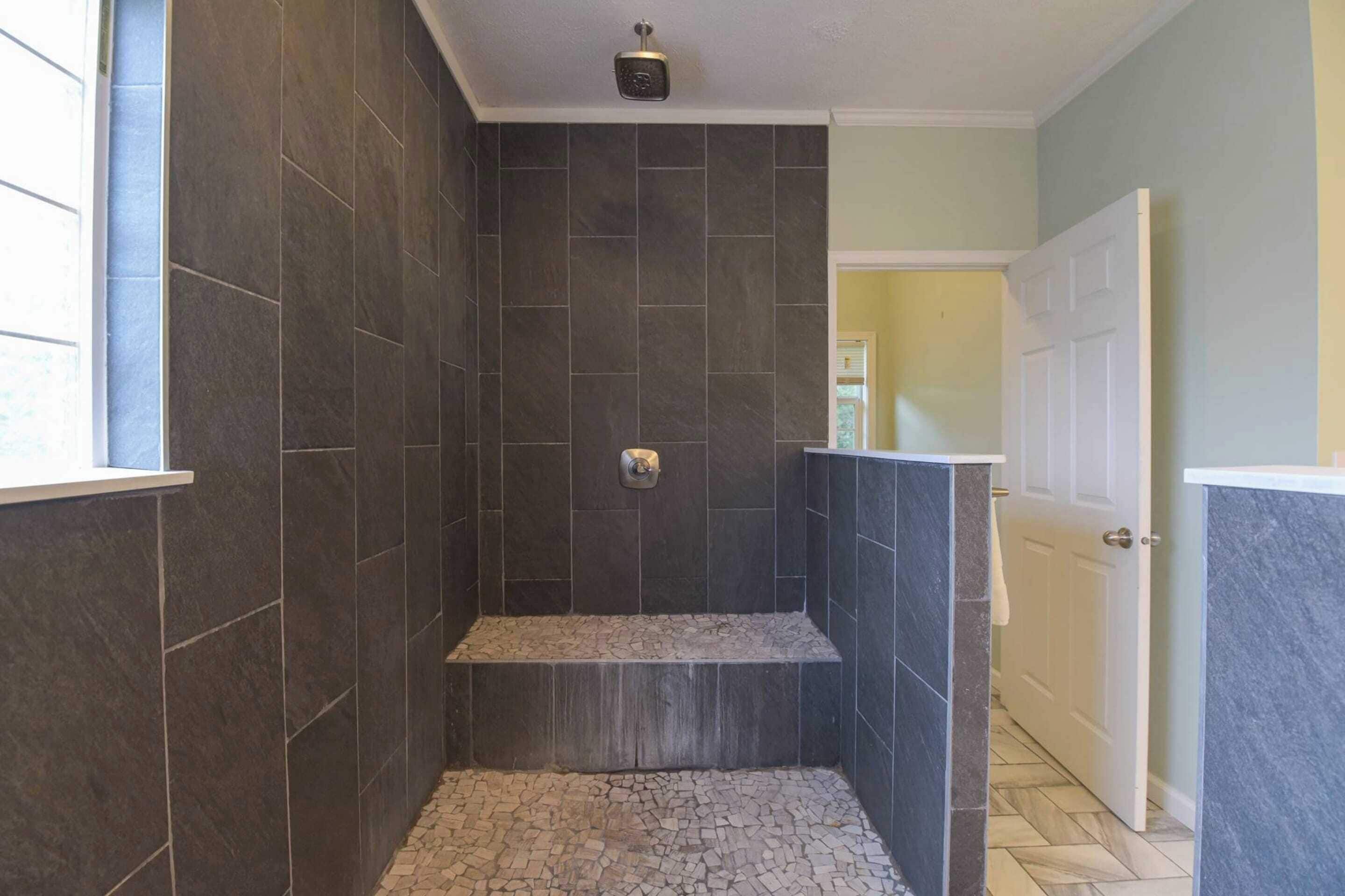 A bathroom with dark tiled walls, a shower area, and a small bench.
