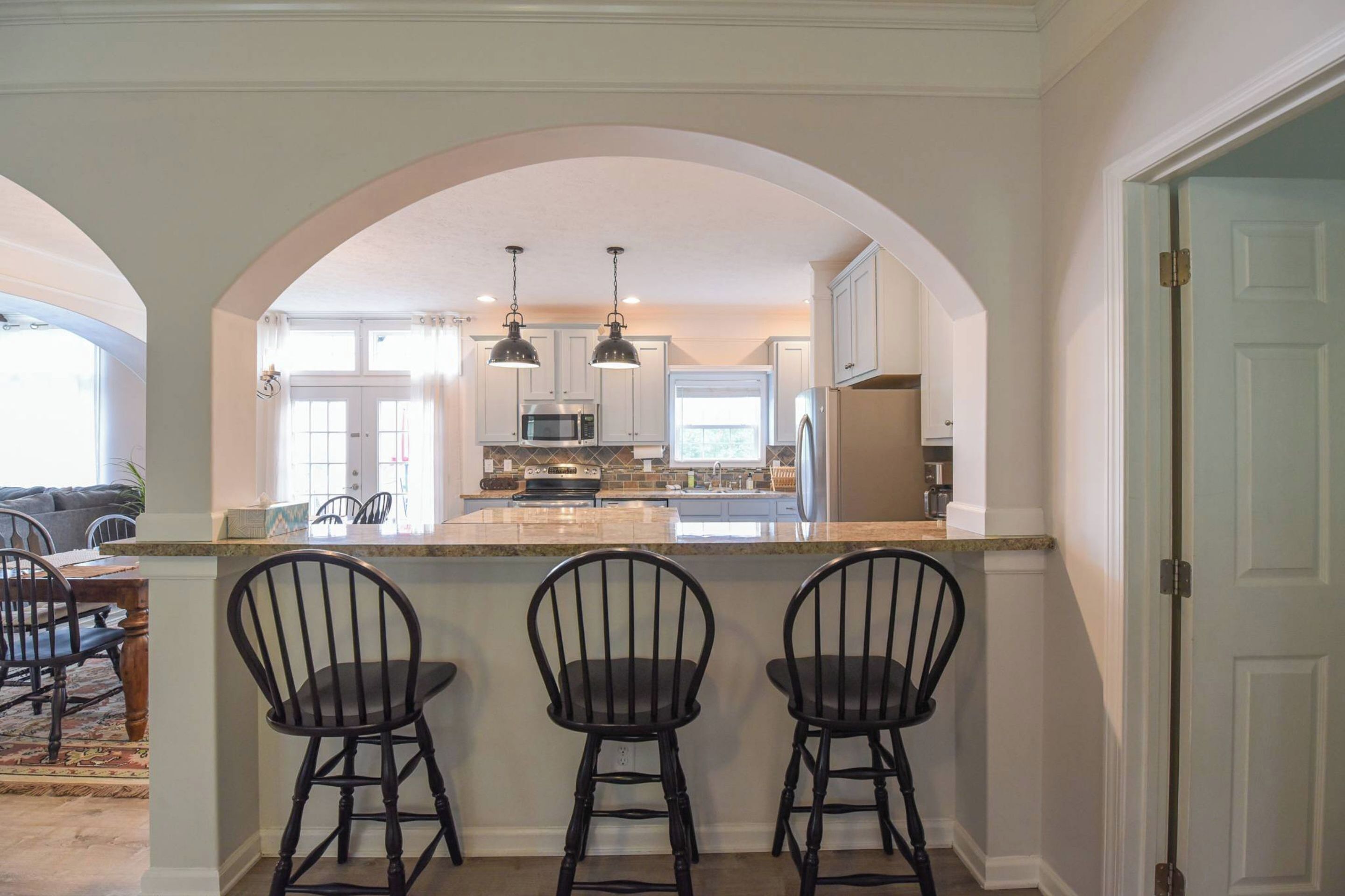 A kitchen with an island, bar stools, pendant lights, and a view through an archway.