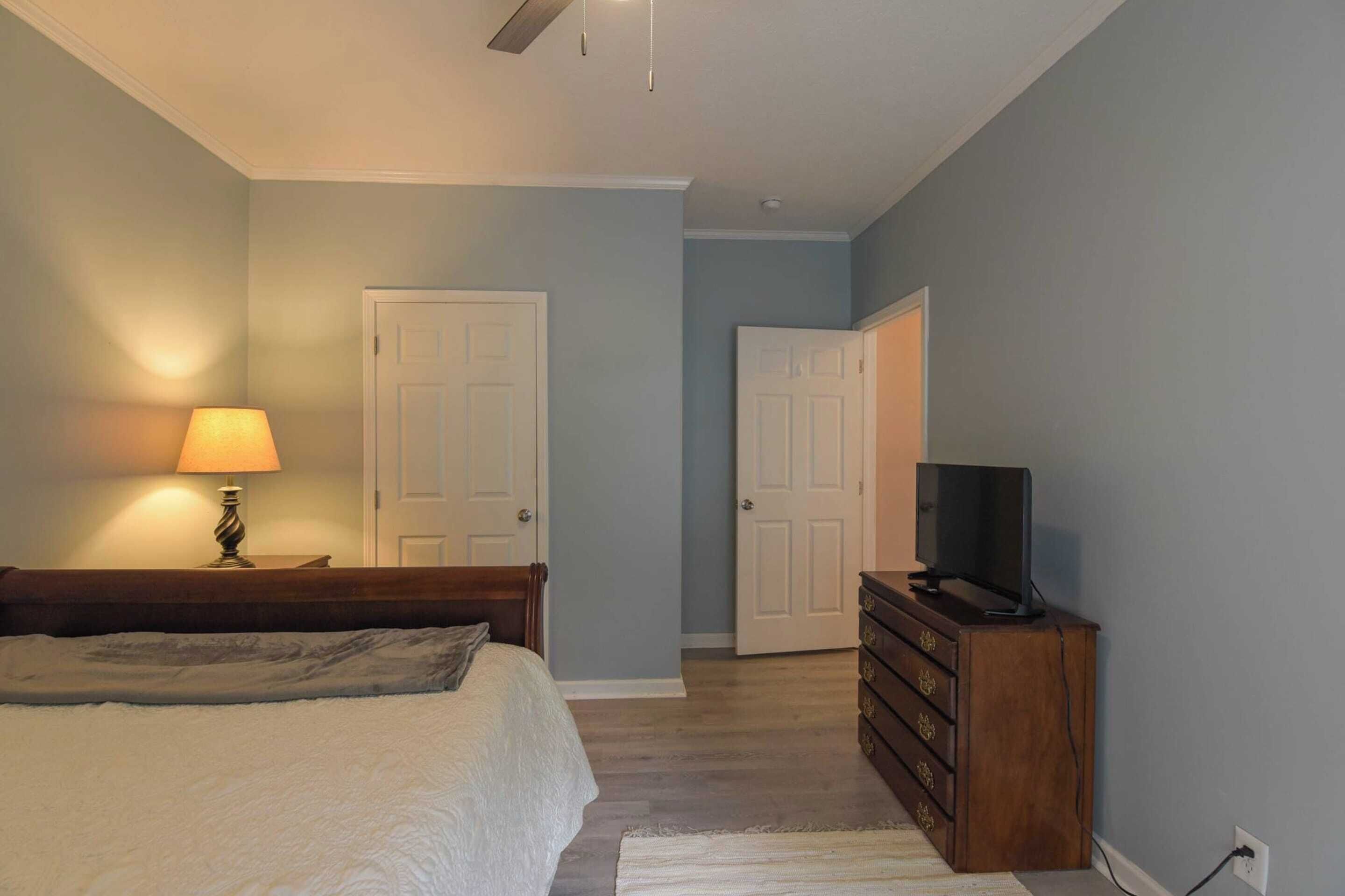 A bedroom with a bed, a dresser, a television, and two doors.