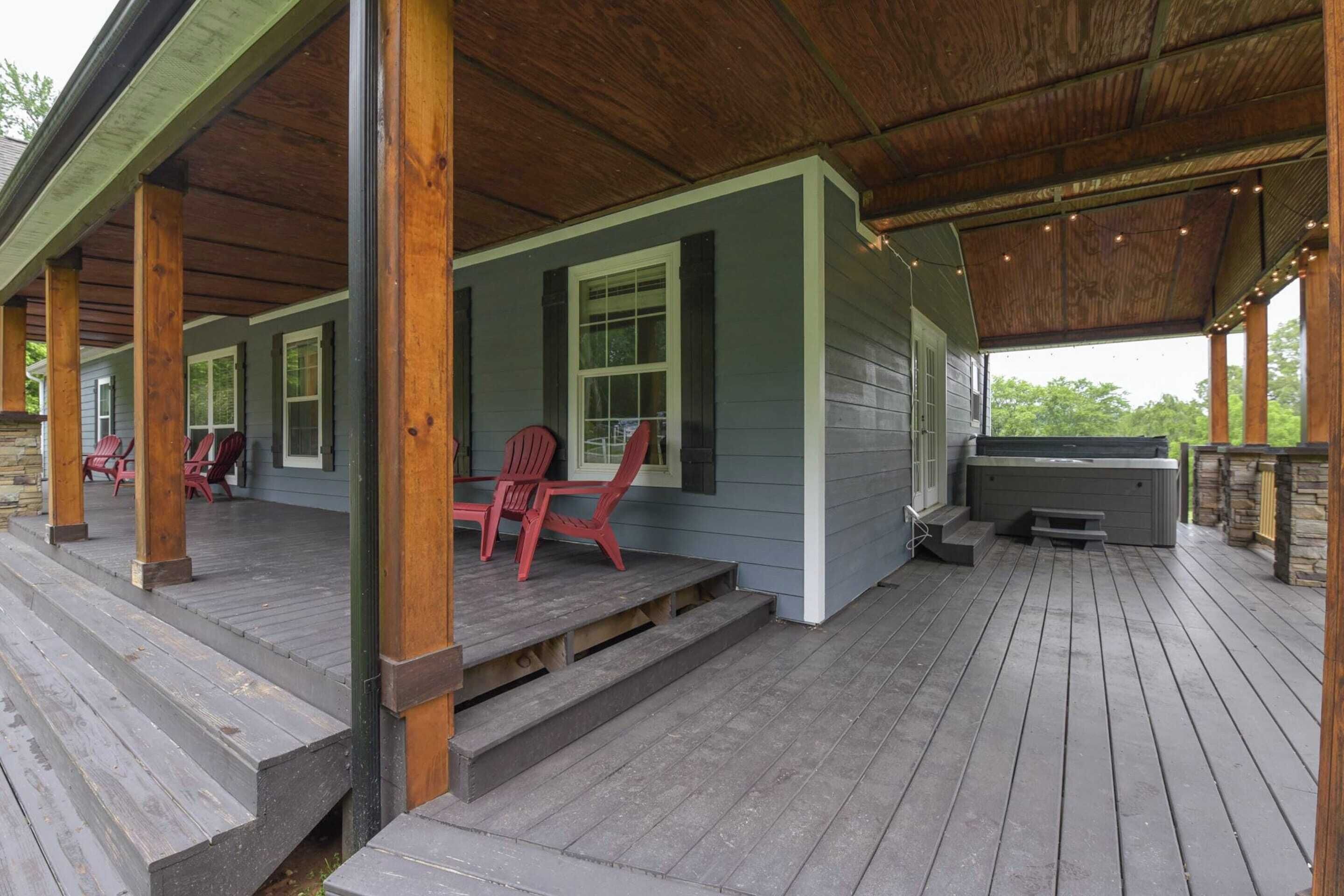 A covered porch with wooden flooring and steps leading to a seating area with red chairs.