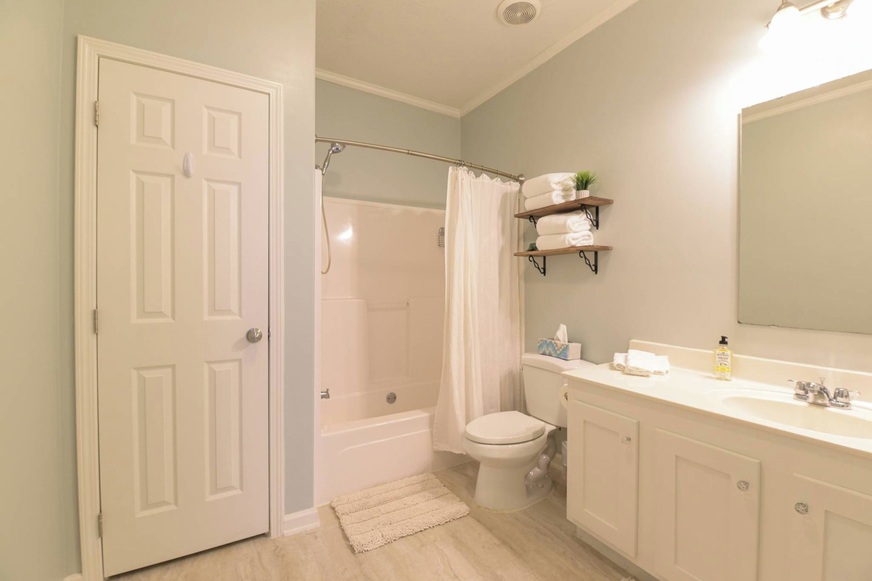 A bathroom with a shower, toilet, sink, and a door.