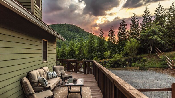 A deck with outdoor furniture, a view of a forested hillside, and a cloudy sky.