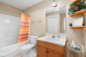 A bathroom with a white bathtub, a white toilet, a wooden vanity with a mirror, and a shower curtain.