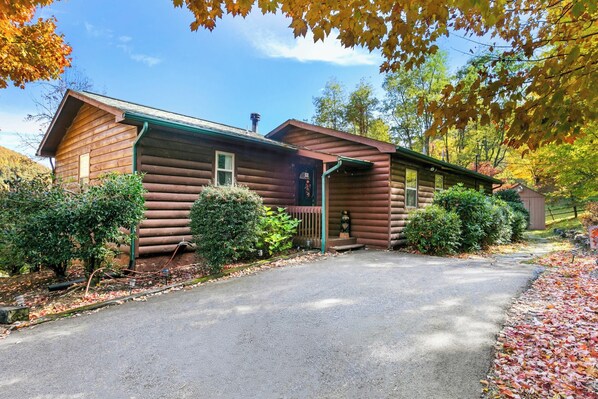 A log cabin with a front porch, surrounded by autumn foliage.