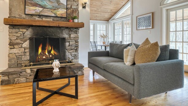 A cozy living room with a stone fireplace, a gray sofa, and a wooden ceiling. - Hamersmith Hollow Retreat by Avantstay Mountain Views (Mars Hill)