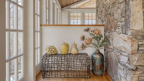 A room with large windows, a stone wall, and a wooden bench with decorative items. - Hamersmith Hollow Retreat by Avantstay Mountain Views (Mars Hill)
