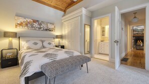 Ein Schlafzimmer mit Bett, Nachttischen, einer Bank, einem Gemälde und einem Kamin.