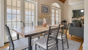 A dining area with a wooden table and chairs, a vase with flowers, and a kitchen in the background. - Hamersmith Hollow Retreat by Avantstay Mountain Views (Mars Hill)