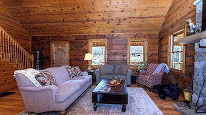 A log cabin interior with a sofa, armchair, coffee table, and fireplace.