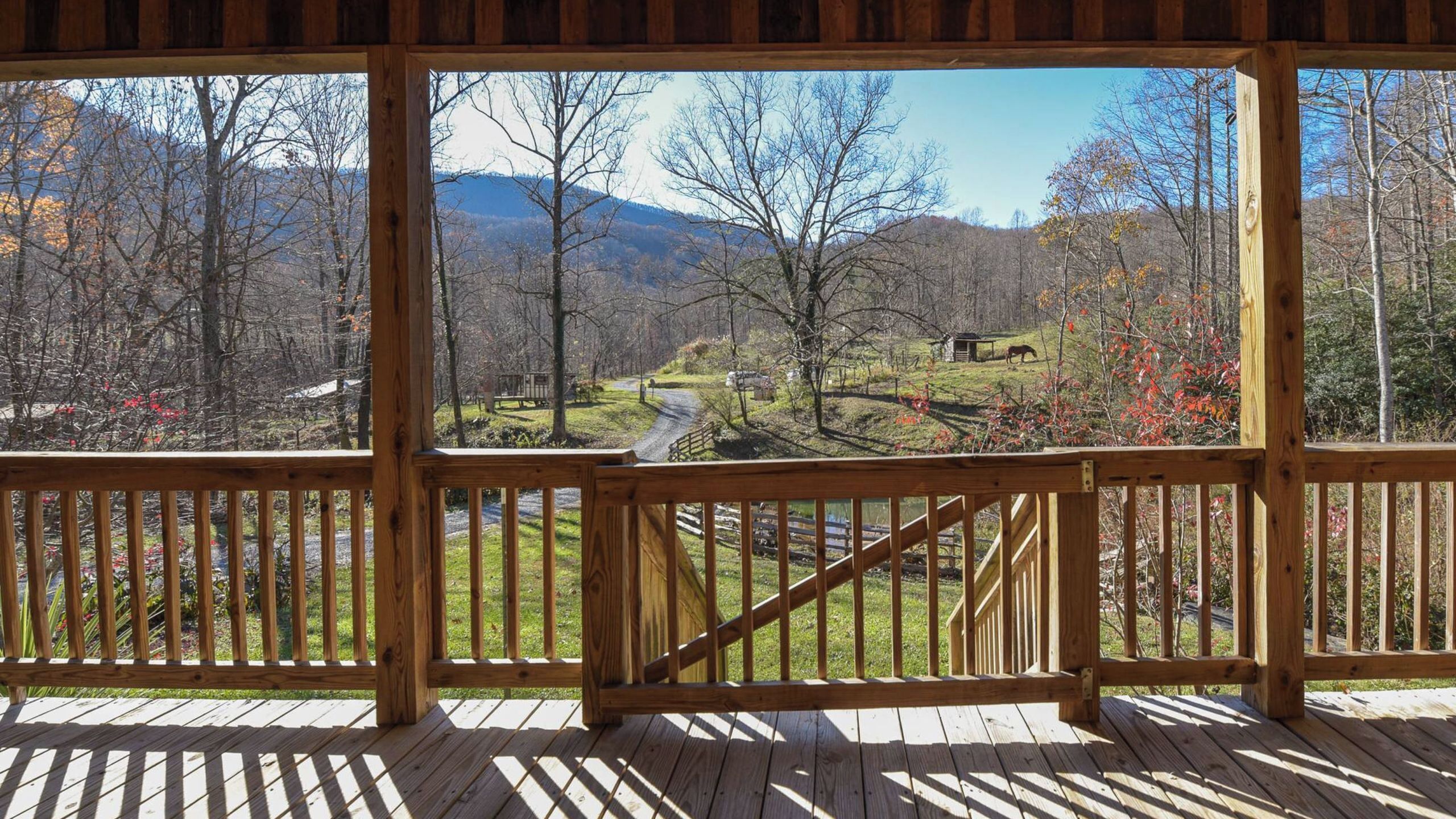 A wooden deck with a view of a rural landscape, including trees, a road, and a small building.