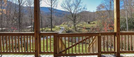 A wooden deck with a view of a rural landscape, including trees, a road, and a small building.