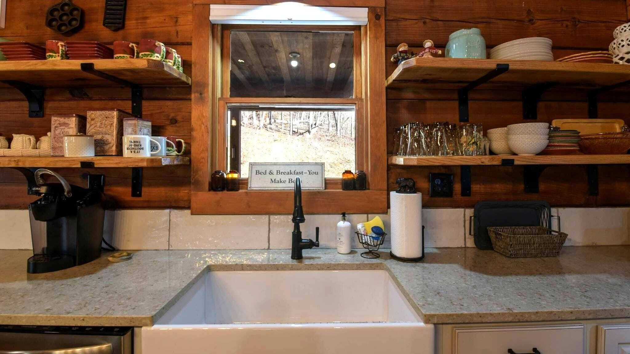 A kitchen with a sink, coffee maker, and shelves with various items.