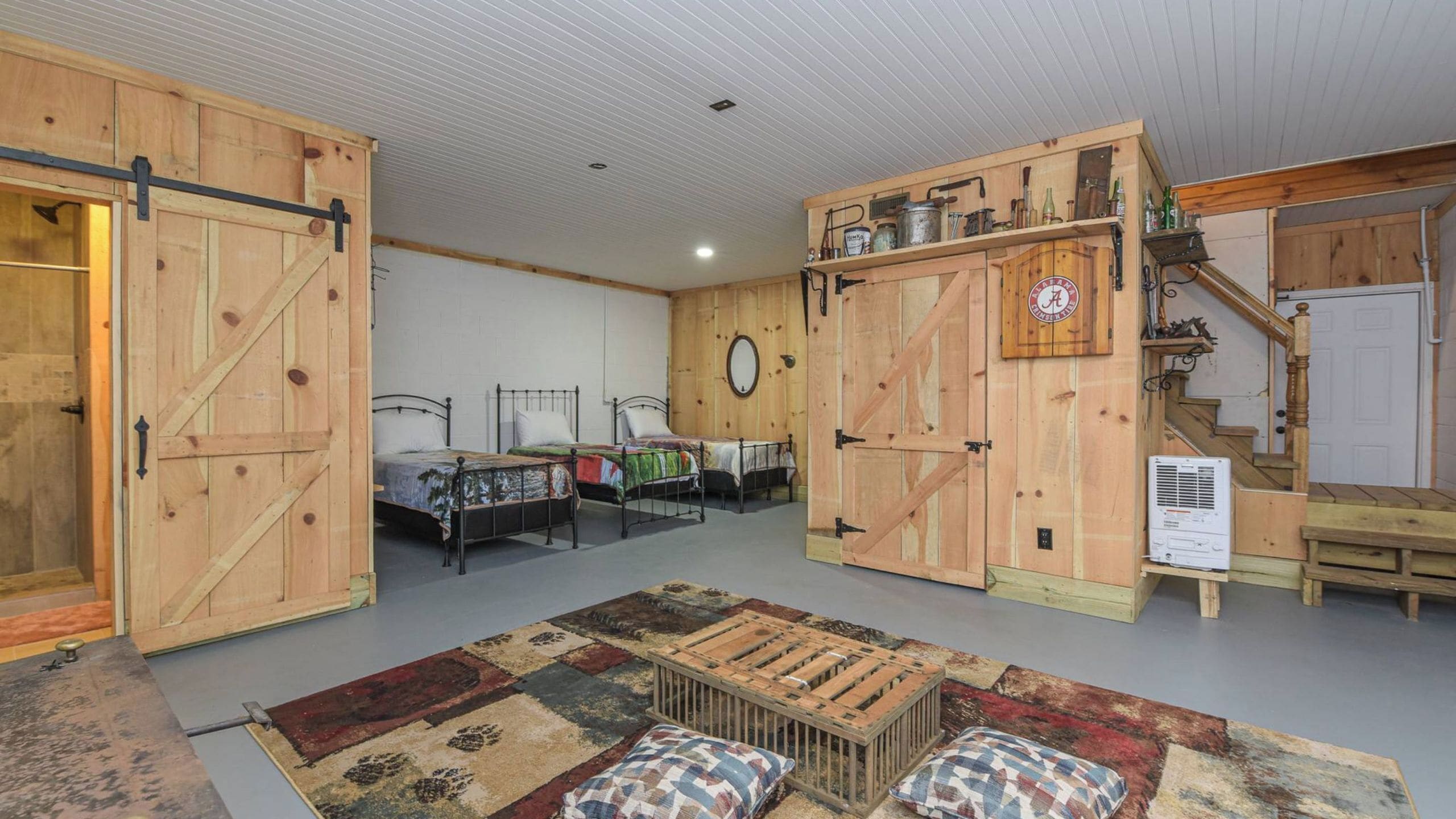 A rustic room with wooden walls, two beds, a staircase, and a small kitchen area.