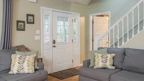 A living room with two grey sofas, a white door, and a staircase. - Asheville Cottage Retreat by Avantstay A+ Charm (Fairview)