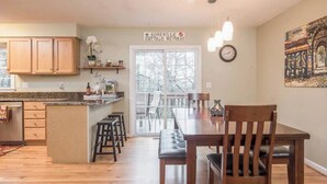 A kitchen with wooden cabinets, a dining table with chairs, a bench, and a sign reading 'ASHEVILLE COTTAGE RETREAT.' - Asheville Cottage Retreat by Avantstay A+ Charm (Fairview)