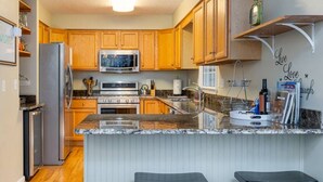 A kitchen with wooden cabinets, a stainless steel refrigerator, a microwave, an oven, and a granite countertop. - Asheville Cottage Retreat by Avantstay A+ Charm (Fairview)