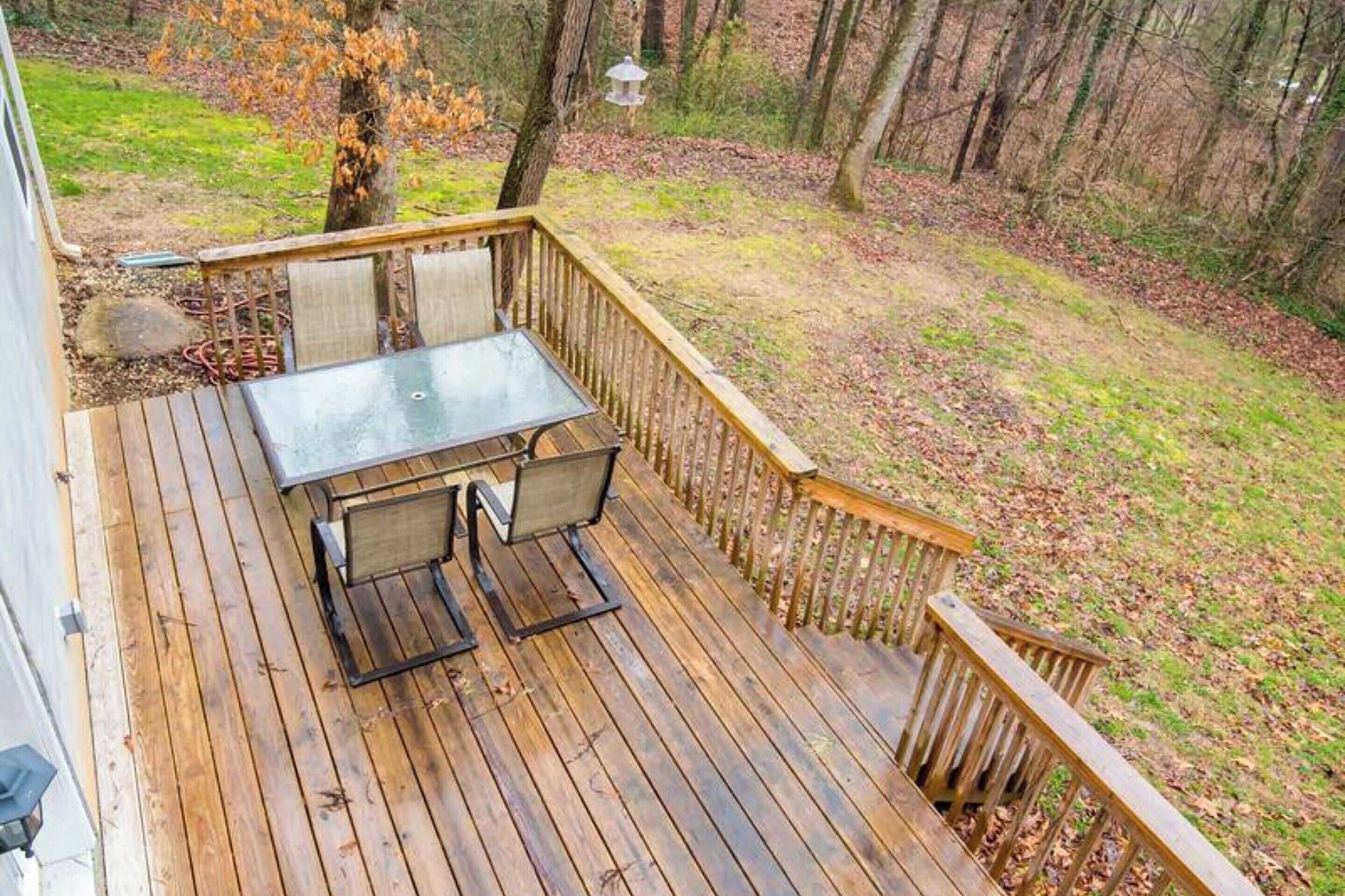 A wooden deck with a glass table and chairs, surrounded by a wooden railing.
